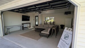 A garage with a seating area, a table, and a projector. - Walk to Lambeau! Sleeps 8• Fire Pit • Party Garage • Parking for 6 vehicles (Ashwaubenon)