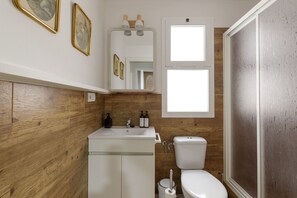 Ein Badezimmer mit Holzvertäfelung, einem weißen Waschbecken, einer Toilette und einem Spiegel mit gerahmten Bildern.