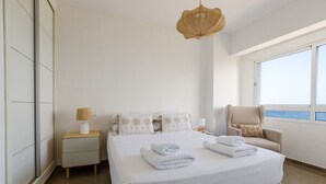 Een moderne slaapkamer met een groot bed, een stoel, een nachtkastje en een raam met uitzicht.