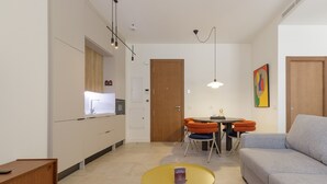 A modern living room with a sofa, a coffee table, and a dining area with orange chairs.