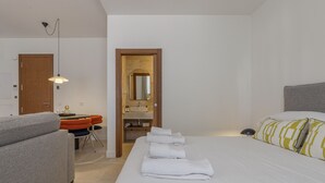 A hotel room with a bed, a desk with a chair, a bathroom with a sink and mirror, and a door.