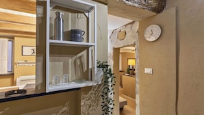 Une pièce avec une étagère contenant une bouteille d’eau en métal, une tasse et des verres. Il y a une horloge au mur et une plante sur le sol.