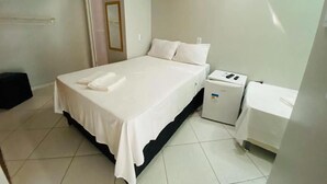 Une chambre d’hôtel propre et moderne, avec un lit bien fait, une table de chevet, un petit bureau et une chaise.