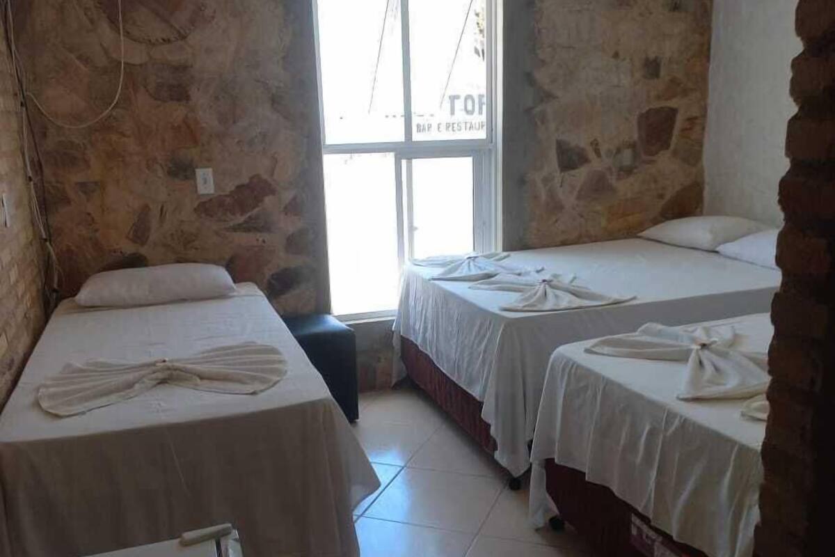 A room with three beds, a tiled floor, stone walls, and a window with a sign reading "TOF BAR E RESTAUP".