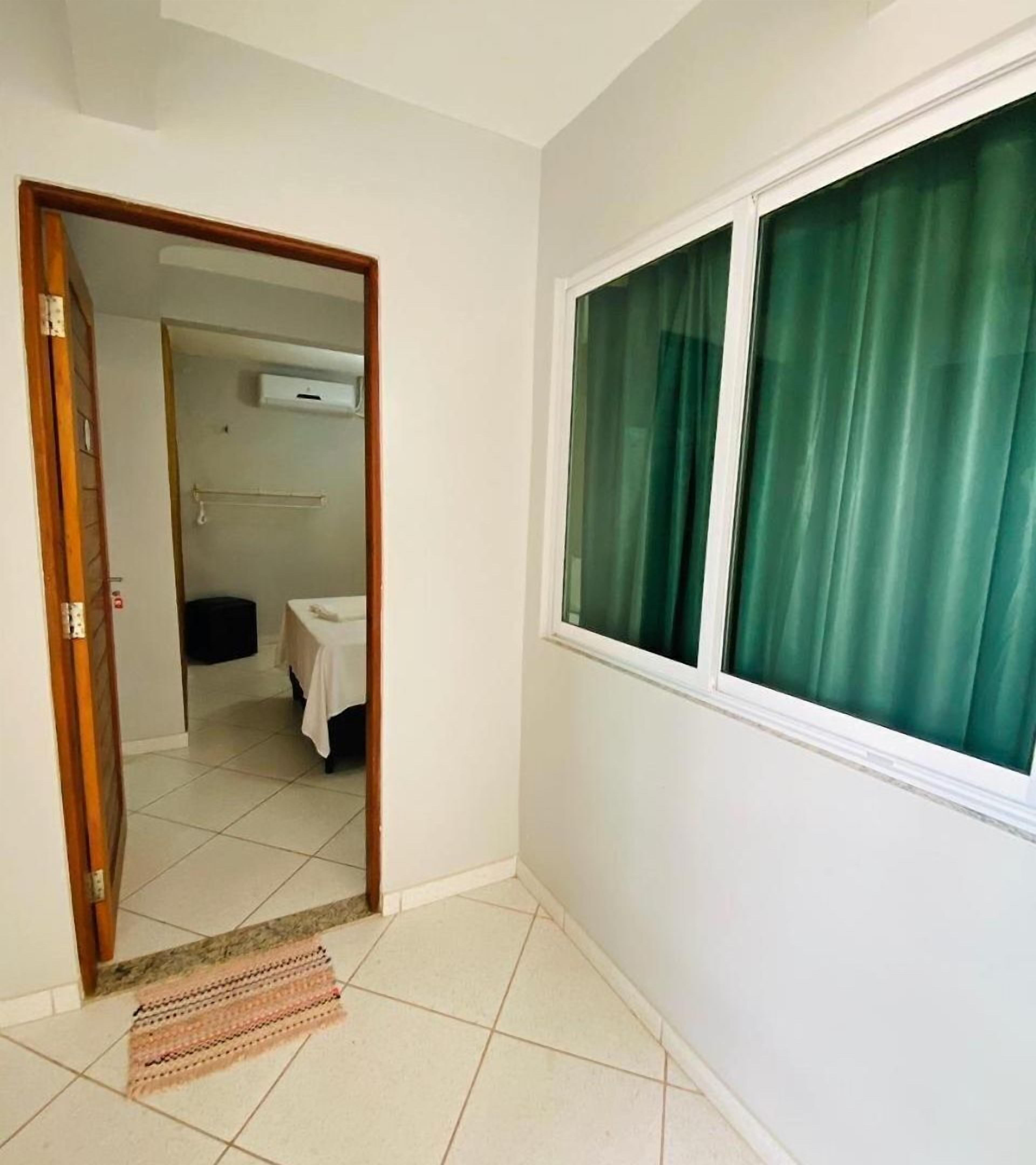 A room with a large window, a door leading to another room, and a tiled floor.