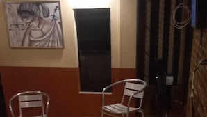 Une pièce avec une table jaune, deux chaises en métal, un tableau au mur et une fenêtre.