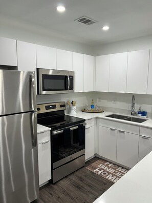 A modern kitchen with stainless steel appliances, white cabinetry, and a wooden floor.