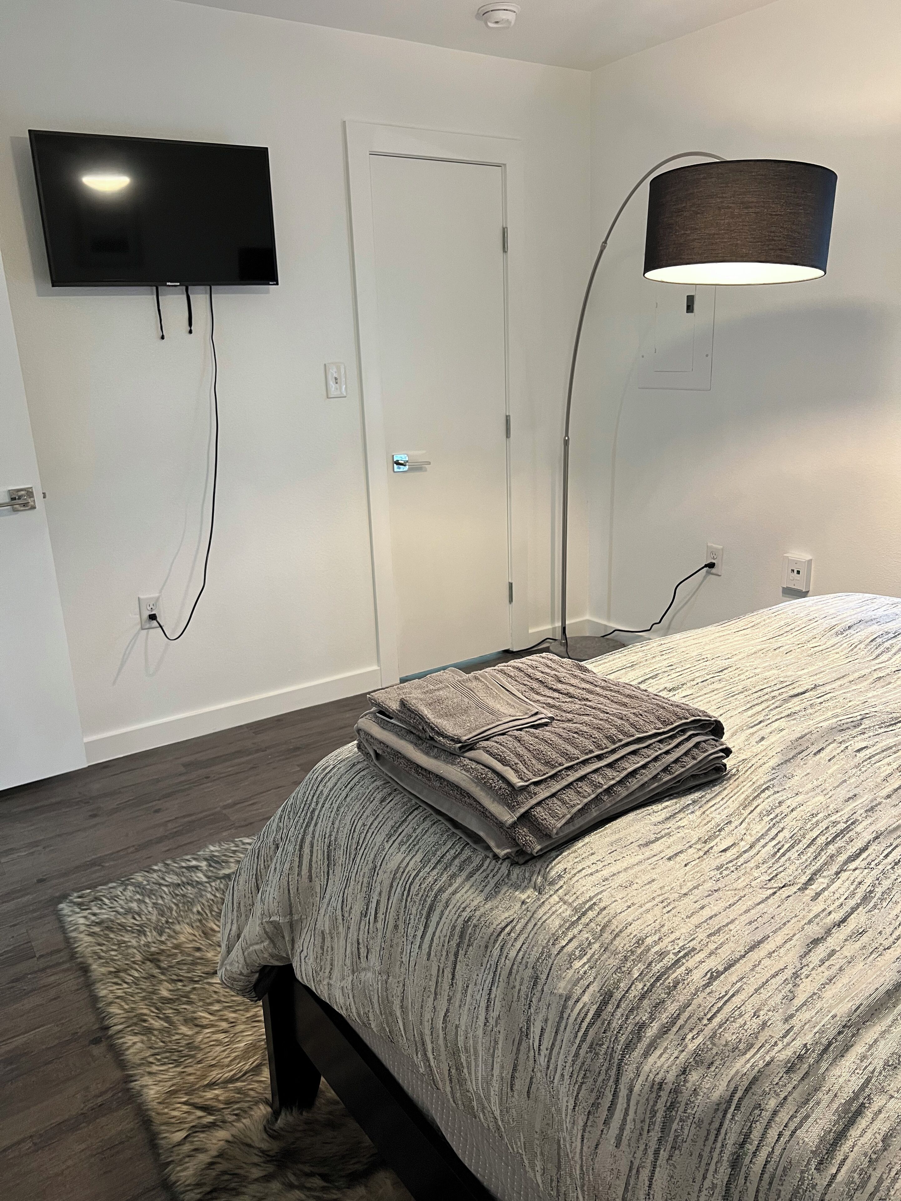 Ein Schlafzimmer mit einem Bett, einem an der Wand befestigten Flachbildfernseher, einer Tür und einer Lampe.