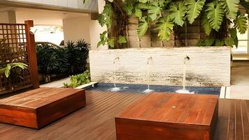 A wooden bench area with a water feature and a planter with large leaves.