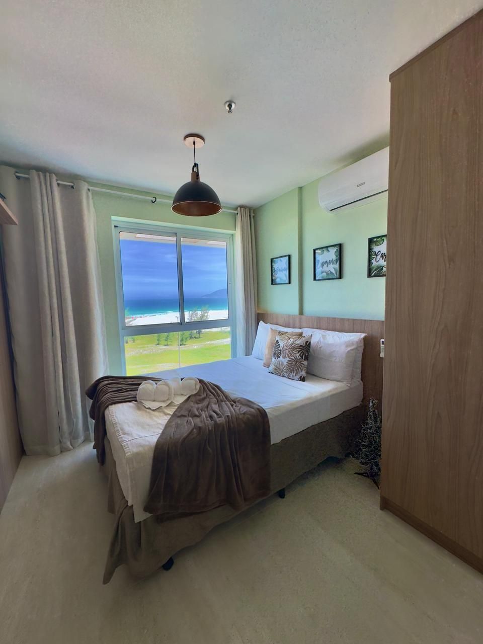 Een slaapkamer met een bed, gordijnen, een raam met uitzicht, een plafondlamp en een aan de muur bevestigde airconditioner.