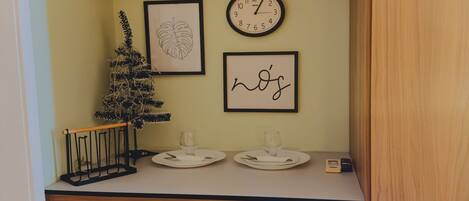 A kitchen area with a microwave, a clock, framed artwork, and a small Christmas tree.