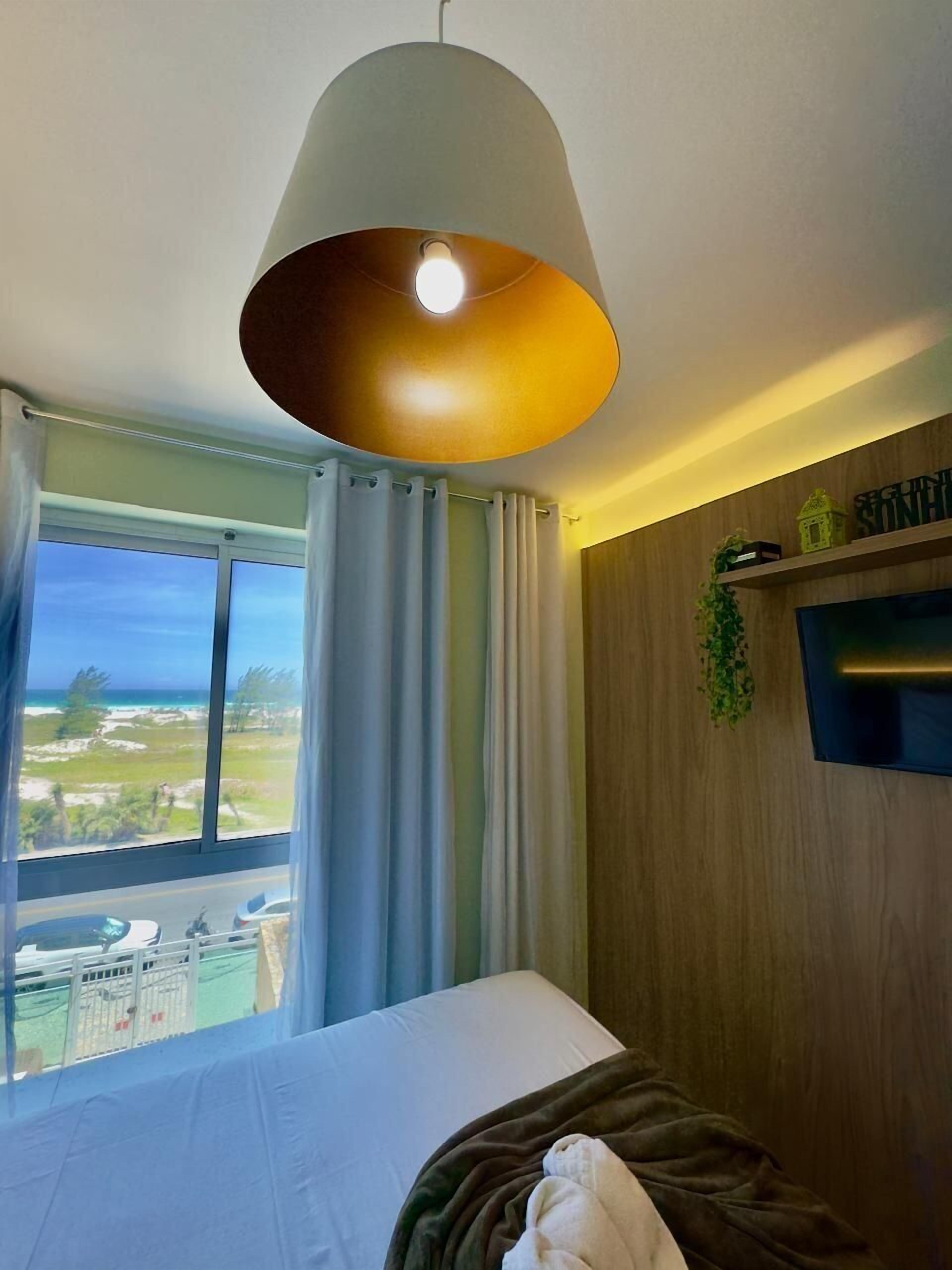 Une chambre d’hôtel avec un lit, une vue sur l’océan, une lampe suspendue et un mur en bois.