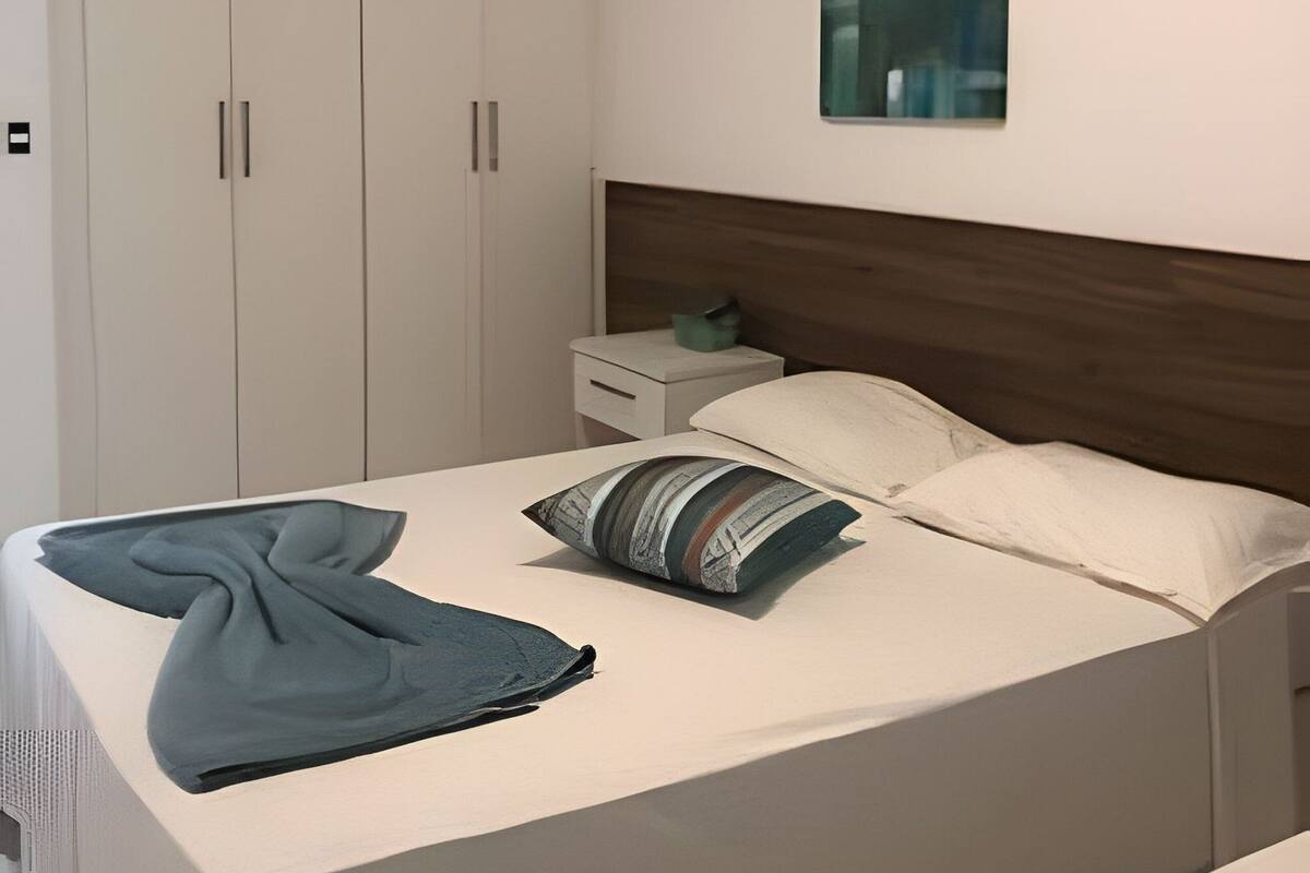 A bedroom with a bed, pillows, a nightstand, a wardrobe, and a painting on the wall.