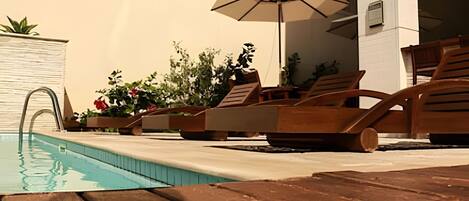 A pool area with lounge chairs and an umbrella.