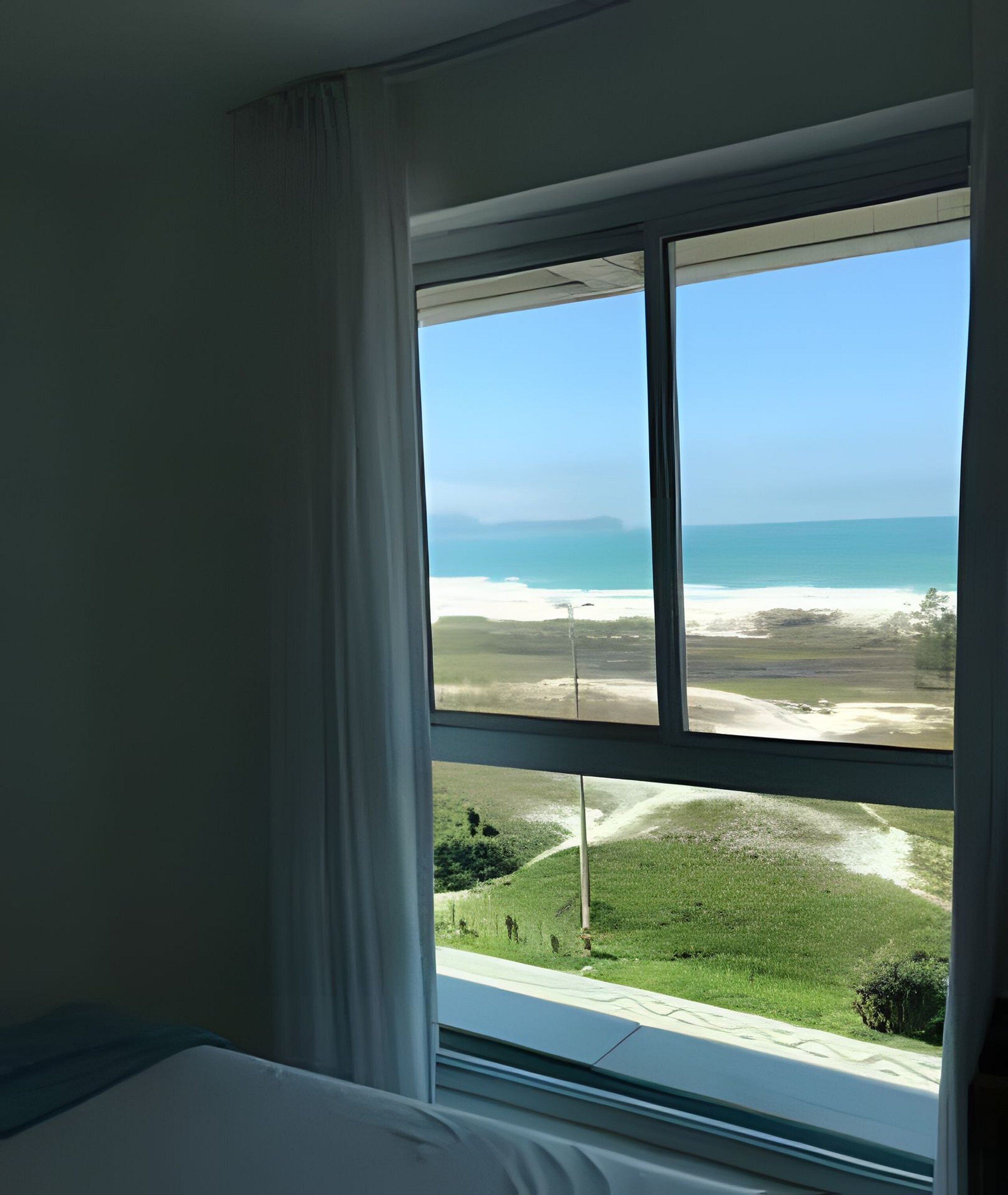 A room with a large window overlooking a beach and ocean.