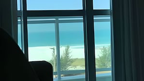 A room with a large window overlooking a beach and ocean. - Flat Mandai Cabo Frio (Cabo Frio)