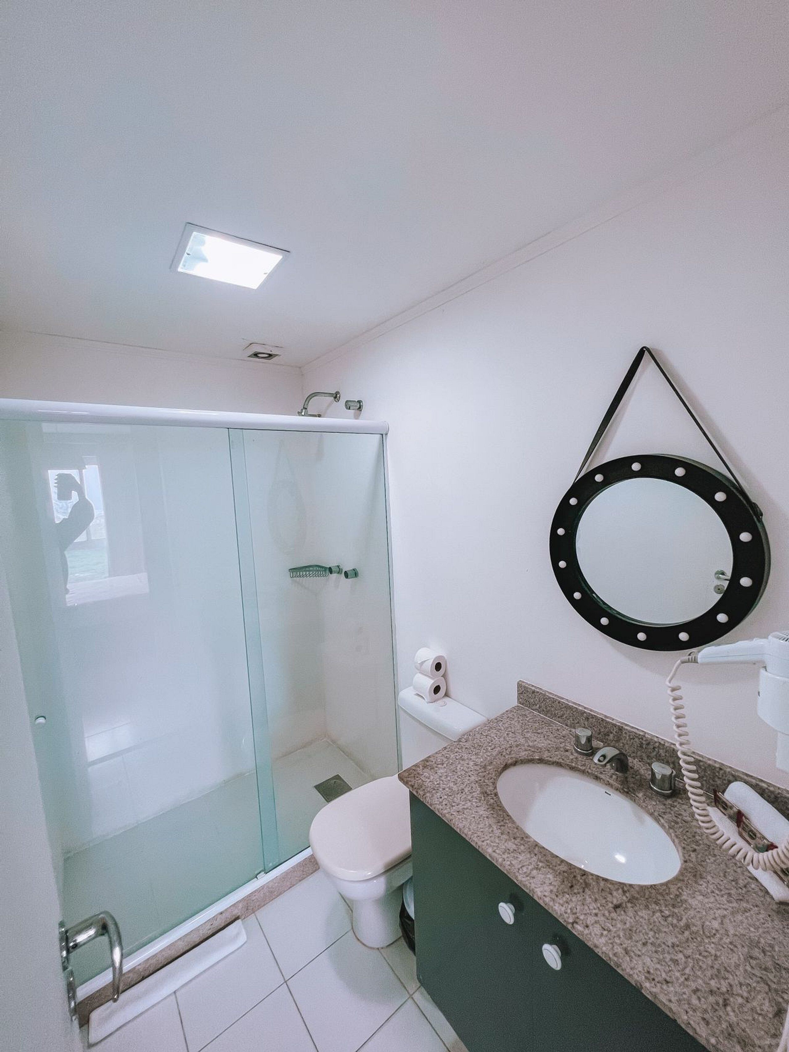 A bathroom with a glass-enclosed shower, a toilet, a sink with a mirror, and a handheld showerhead.