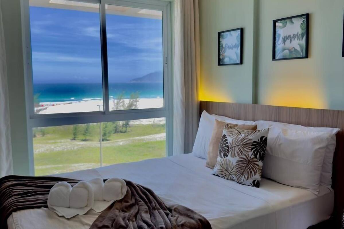A hotel room with a large bed, a view of the beach, and a ceiling fan.