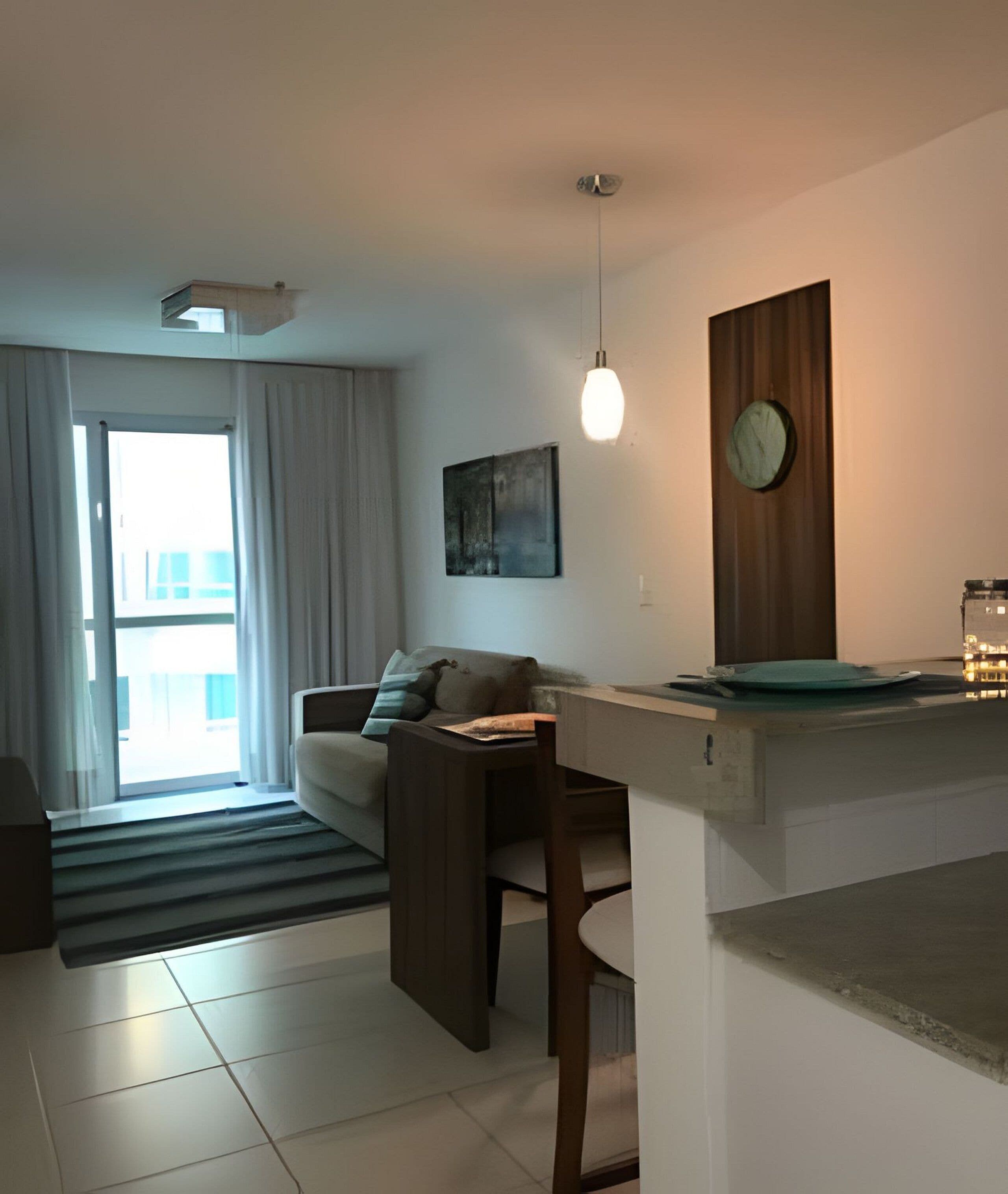 A modern living room with a sofa, a dining table, a pendant light, a clock, and a view through a sliding door.