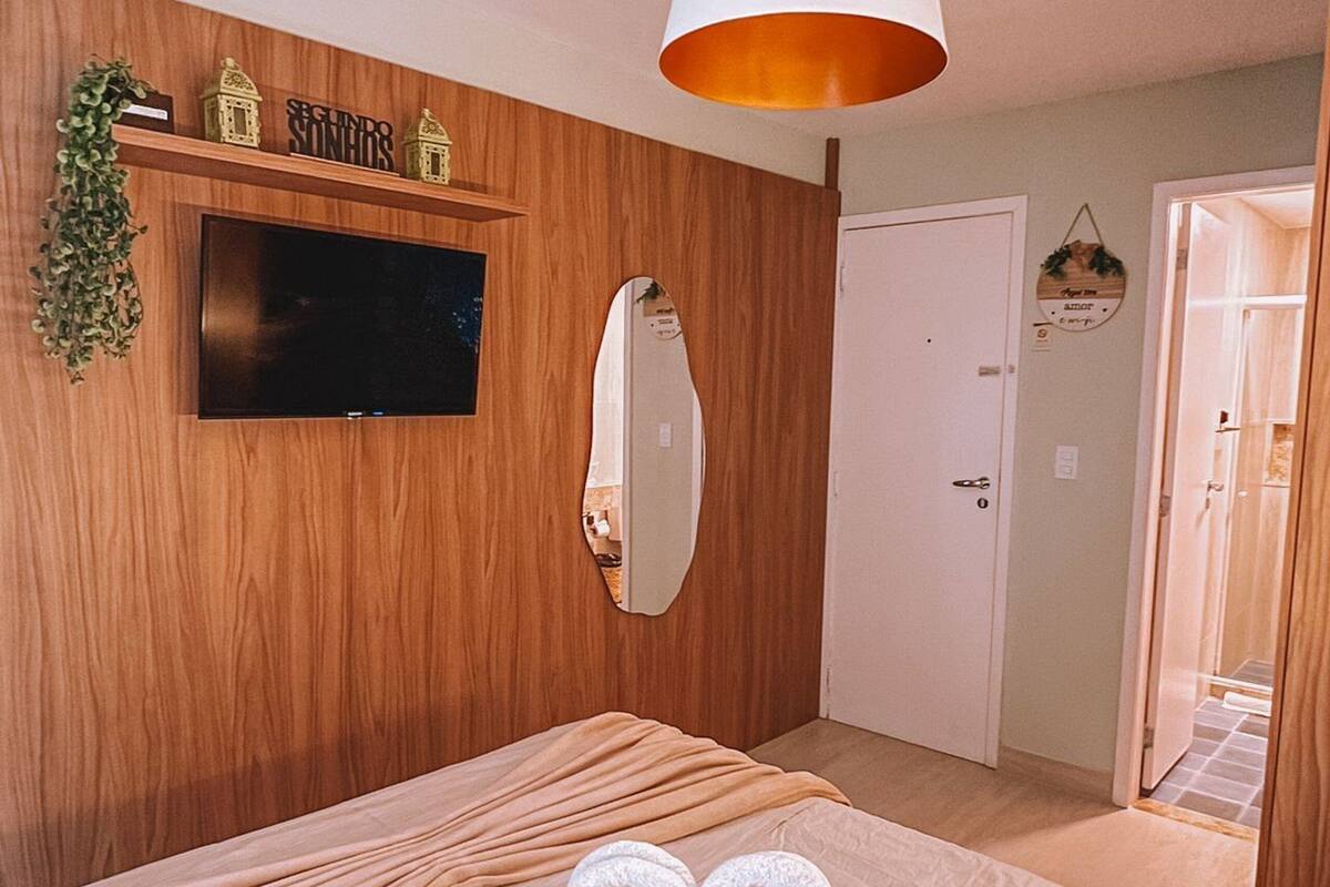 A bedroom with a bed, a television, a mirror, and a hanging light fixture.