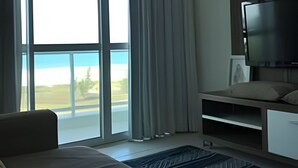 A hotel room with a bed, a TV, a desk, and a view of the outdoors. - Flat Mandai Cabo Frio (Cabo Frio)