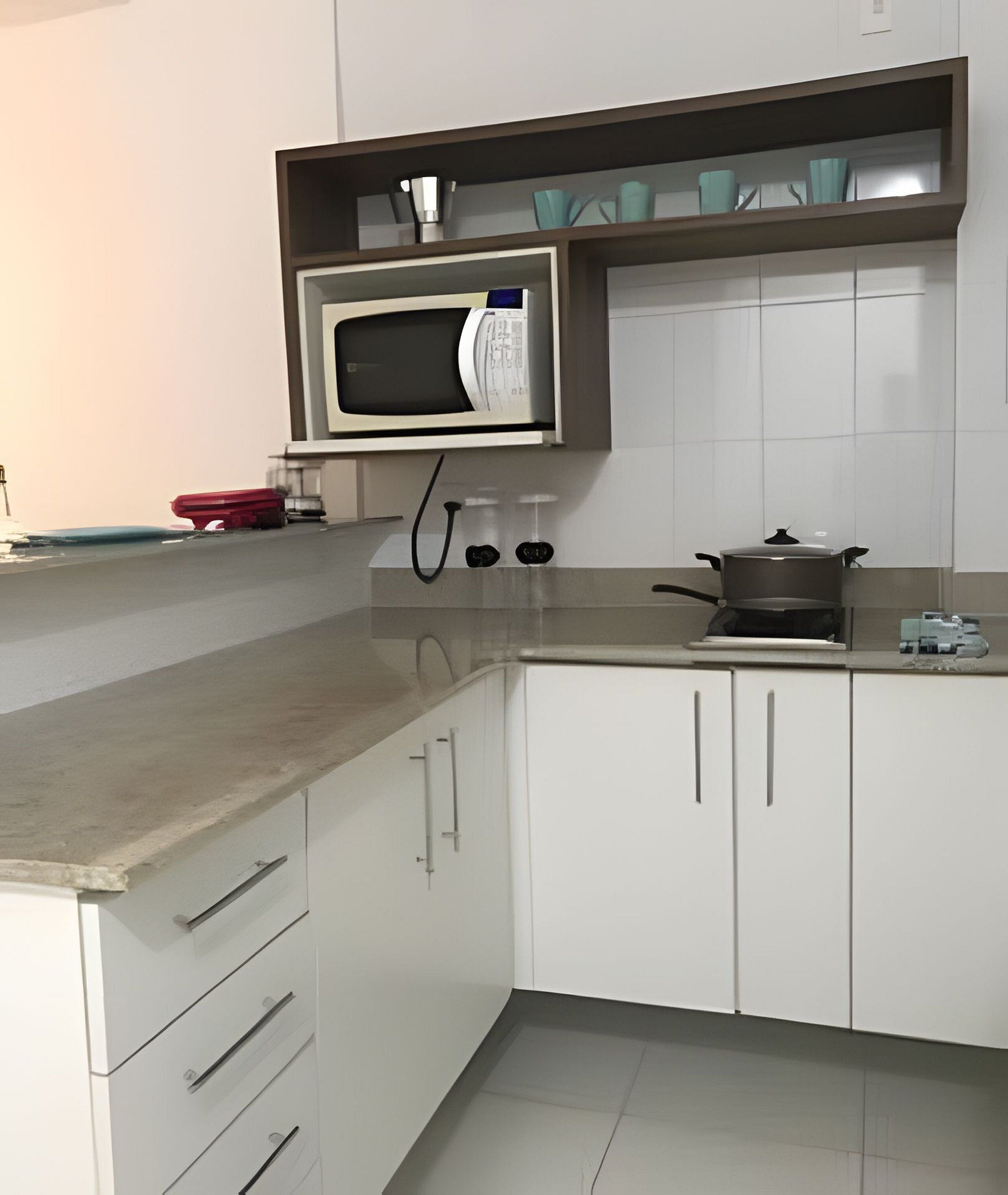 Una cocina con armarios blancos, un microondas, una estufa y una maleta roja sobre la encimera.