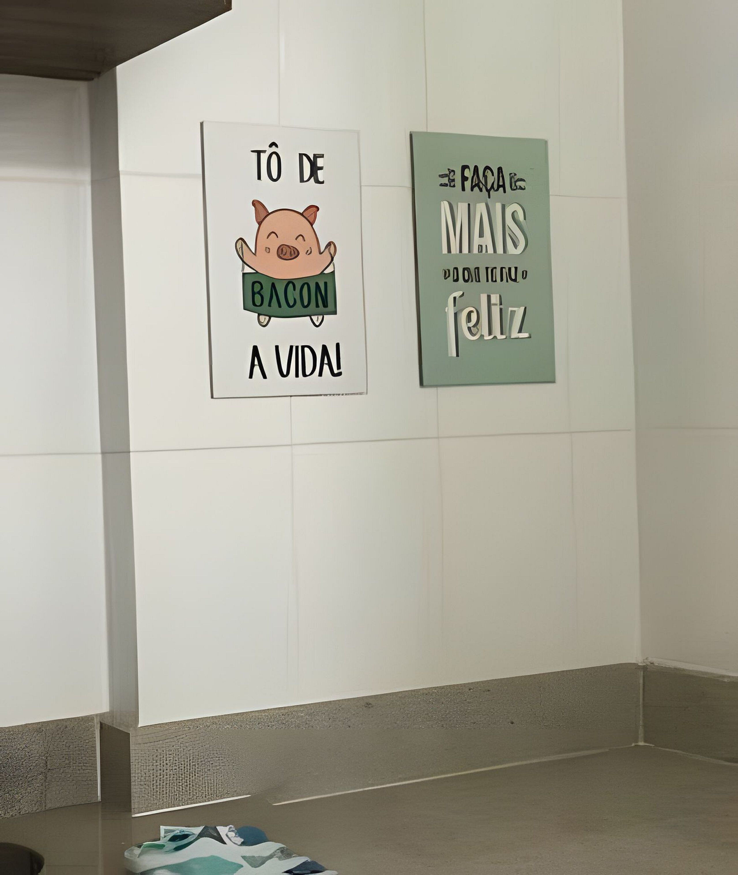 Two wall-mounted signs in a hallway, one with a cartoon pig and the text 'Tô de bacon a vida!' and another with the text 'Faca mais feliz.'