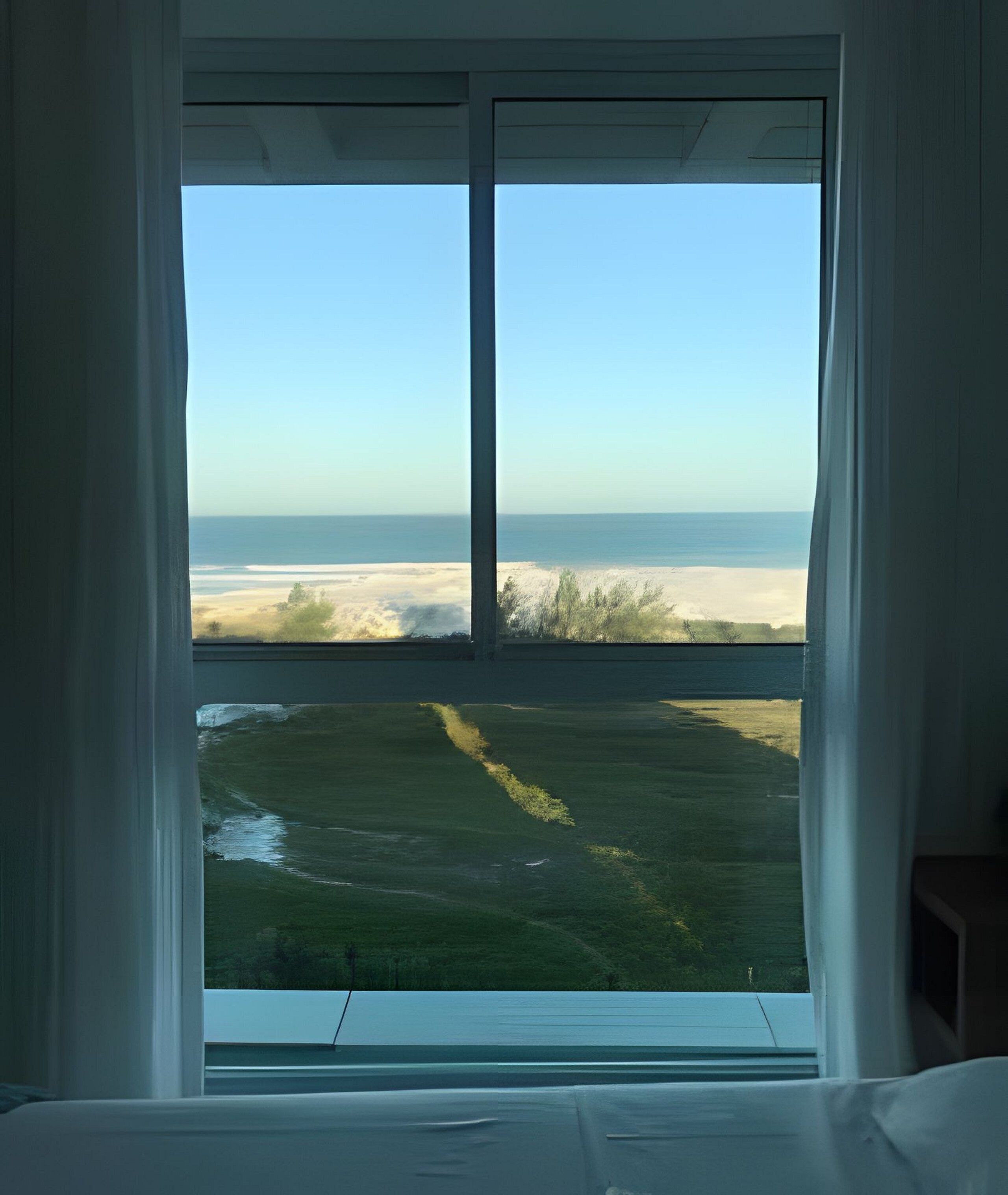 Ein Zimmer mit großem Fenster mit Blick auf Strand und Grünfläche.