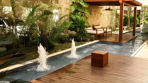 A serene indoor water feature with multiple fountains, surrounded by lush greenery and wooden seating areas. - Flat Mandai Cabo Frio (Cabo Frio)