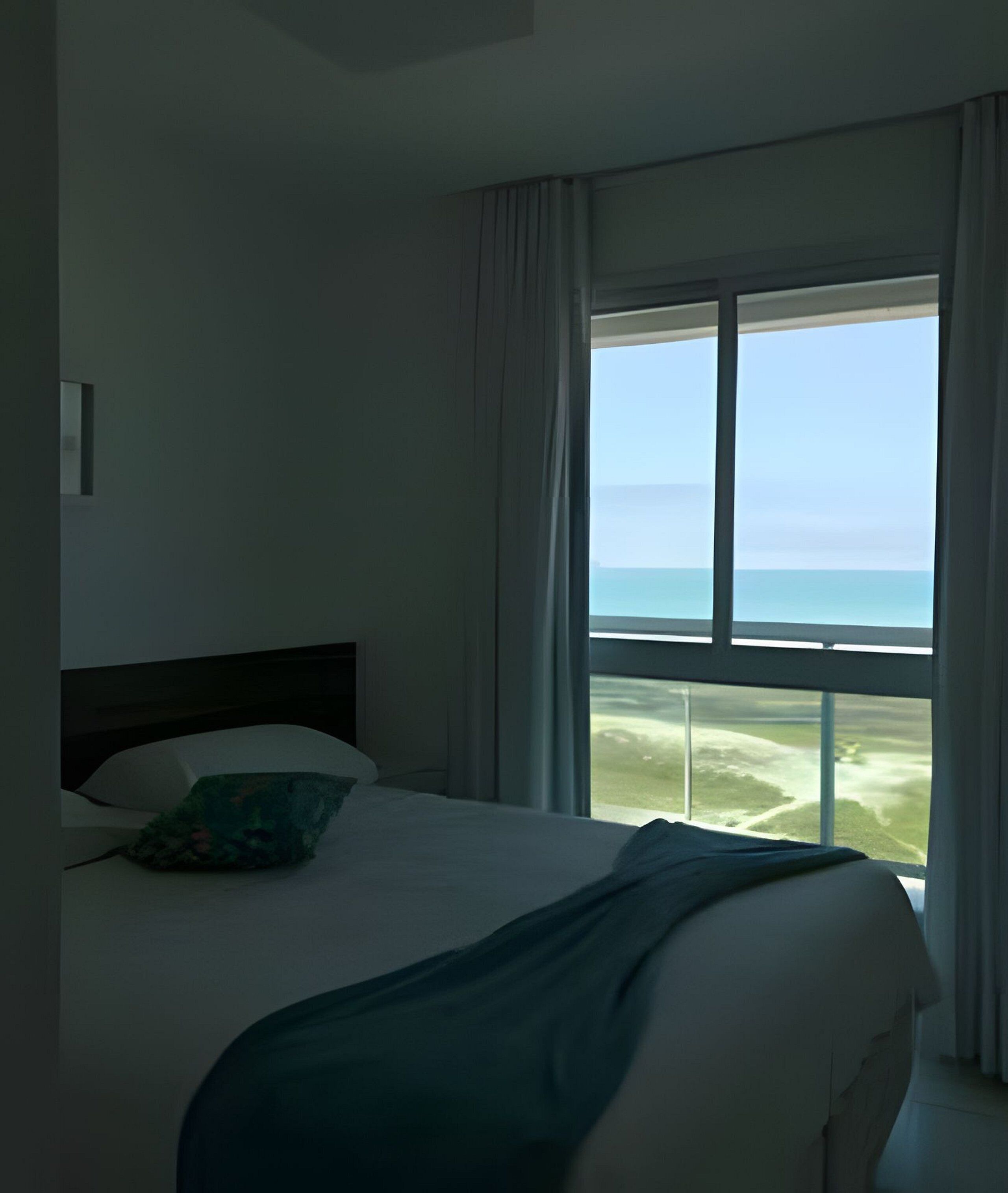 Ein Hotelzimmer mit Bett, Meerblick und einem Vorhangfenster.