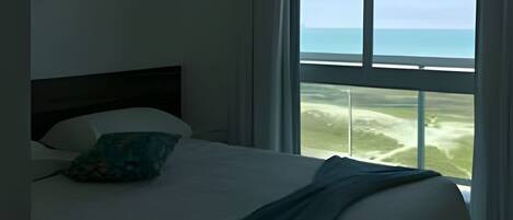 Ein Hotelzimmer mit Bett, Meerblick und einem Vorhangfenster.