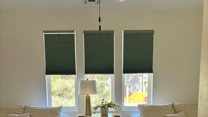 Une chambre avec deux lits, un ventilateur de plafond, une table de chevet avec une lampe et trois fenêtres équipées de stores.
