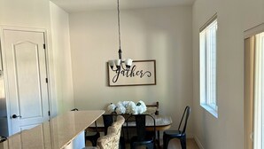 Un espace repas avec une longue table, des chaises à motifs, un lustre et un panneau mural portant l'inscription « Gather ».