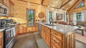Cocina de cabaña de madera con una isla grande, electrodomésticos integrados y una zona de comedor con sofá y mesa.