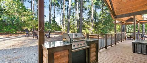 An outdoor deck with a built-in grill, wooden railings, and a view of a forested area.