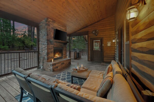 Un espace extérieur accueillant, doté d’une cheminée en pierre, d’une terrasse en bois et offrant une vue sur la forêt environnante.