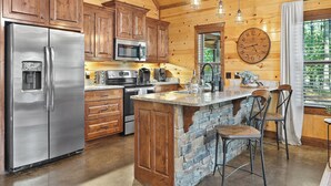 Una cocina con armarios de madera, un refrigerador de acero inoxidable, una isla de piedra y un reloj grande en la pared.