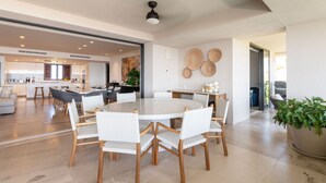 Una cocina moderna con armarios blancos, una isla central y un comedor con mesa redonda y sillas de mimbre.