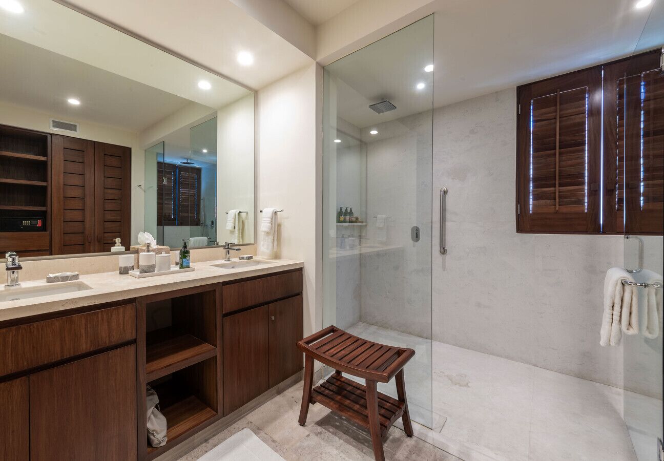Une salle de bain moderne avec un grand miroir, des meubles en bois, une douche en verre et un petit tabouret en bois.