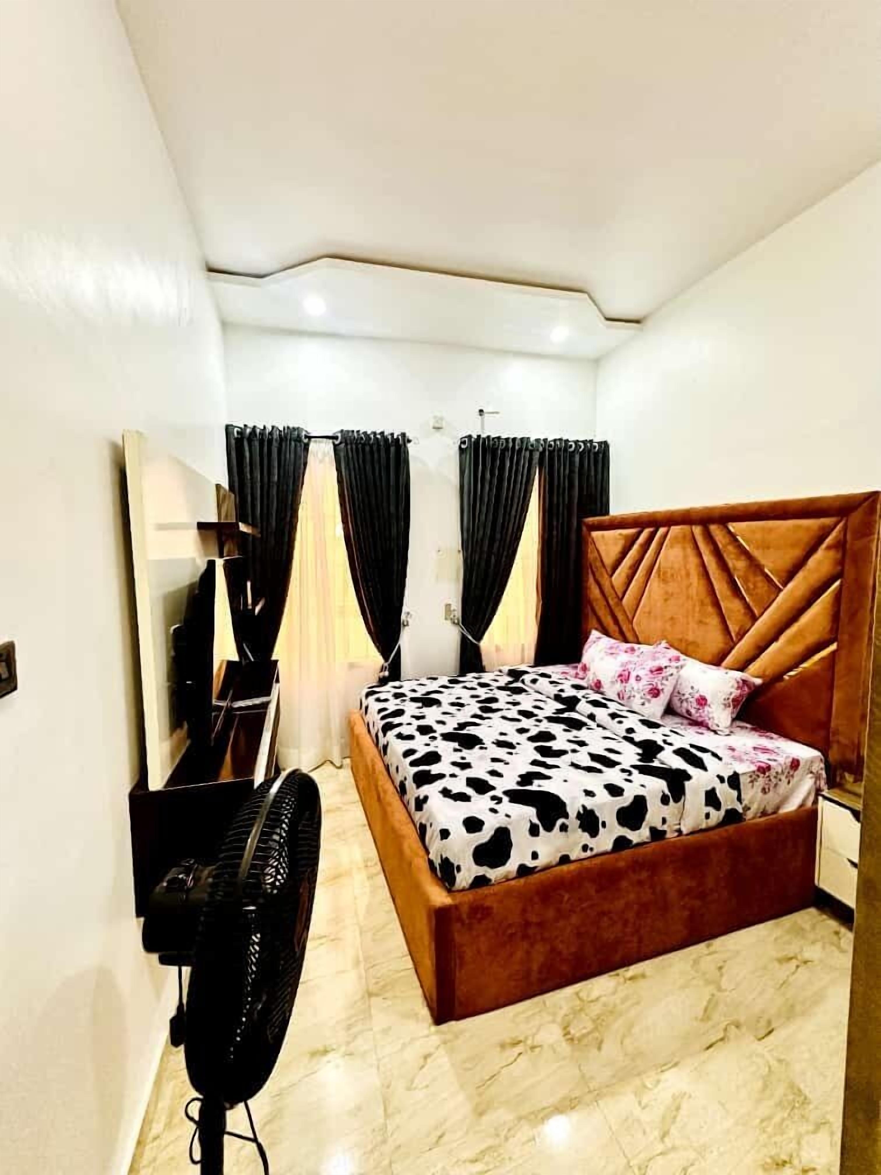 A bedroom with a bed, a fan, a mirror, and curtains.