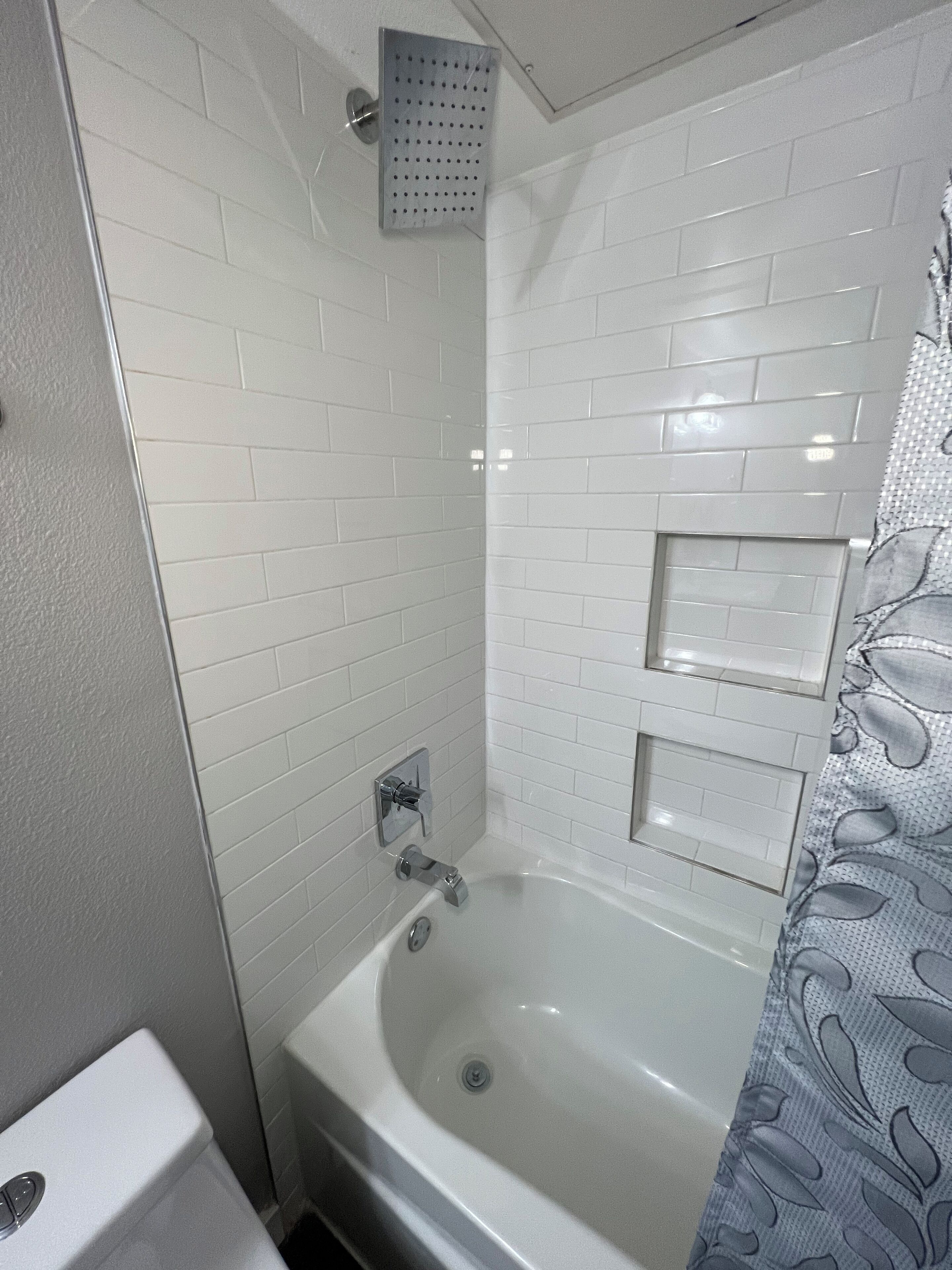 A bathroom with a white bathtub, a showerhead, and a toilet.