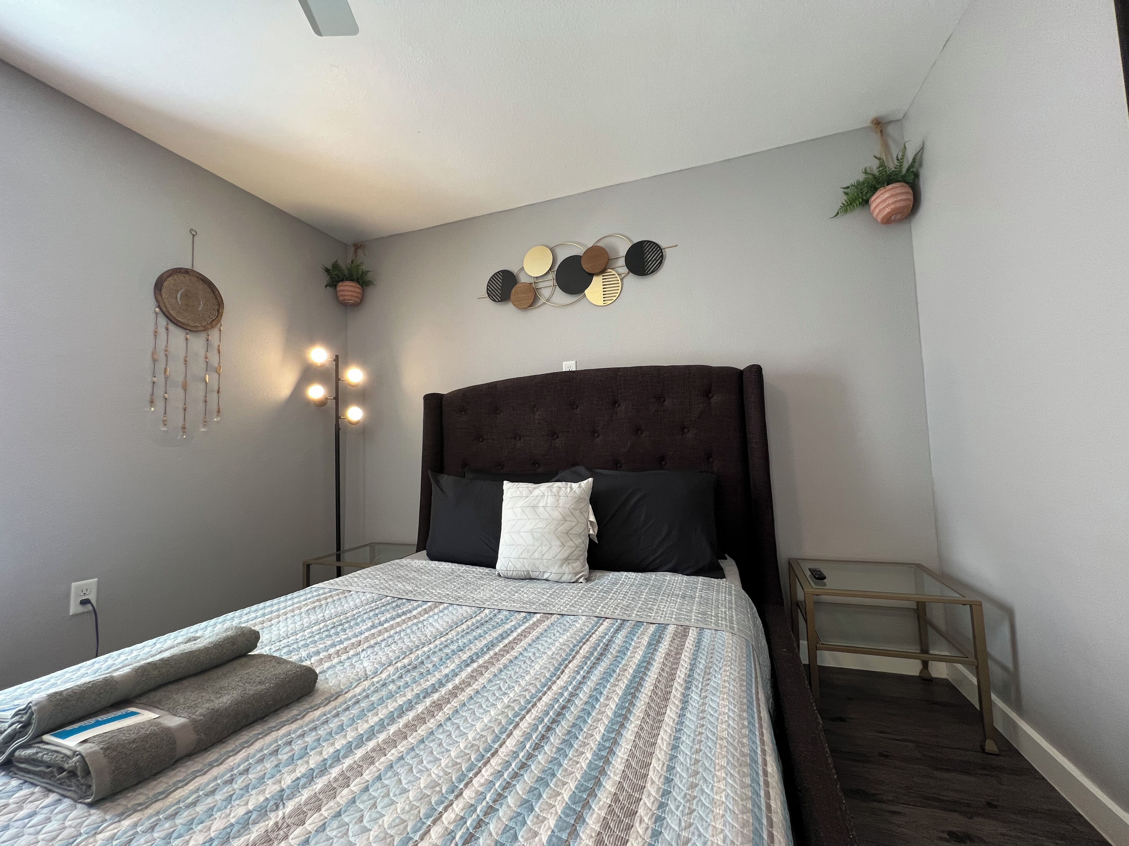 A neatly made bed with a patterned bedspread, a dark headboard, and a bedside table with a lamp.