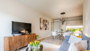 A modern living room with a flat-screen TV, a wooden console, a sofa, and a dining area with a table and chairs. - Luxury Apartment with Elevator and Private Parking (Lucca)