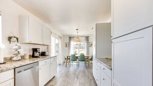 A modern kitchen with white cabinets, a wooden countertop, and a dining area with green chairs. - High-Desert Home w/ Hot Tub & Cowboy Pool (Joshua Tree)
