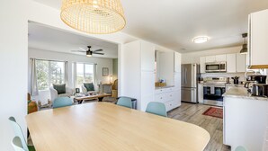 A modern kitchen with white cabinets, stainless steel appliances, and a large wooden dining table. - High-Desert Home w/ Hot Tub & Cowboy Pool (Joshua Tree)