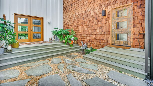 Una casa moderna con rivestimento in legno, una porta vetrata e un vialetto in pietra che conduce all'ingresso.