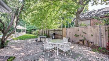 Une terrasse avec une table ronde et des chaises, entourée d’une zone recouverte de gravier et d’une clôture en bois.