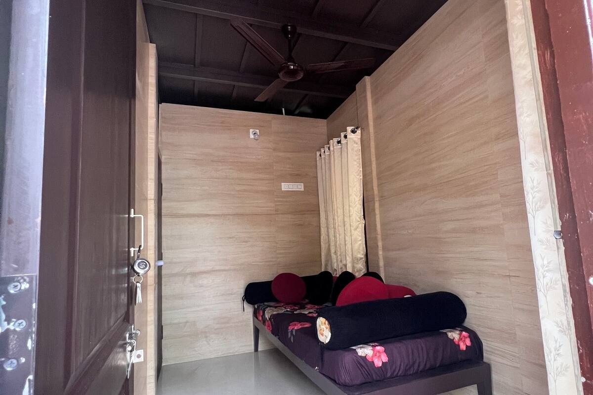 A narrow room with a bed, a ceiling fan, and a door with a lock.