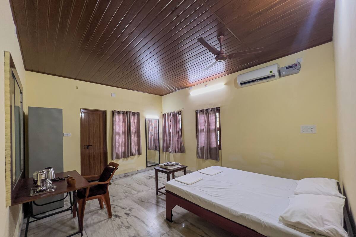A room with a bed, a desk, a chair, a mirror, and an air conditioning unit.