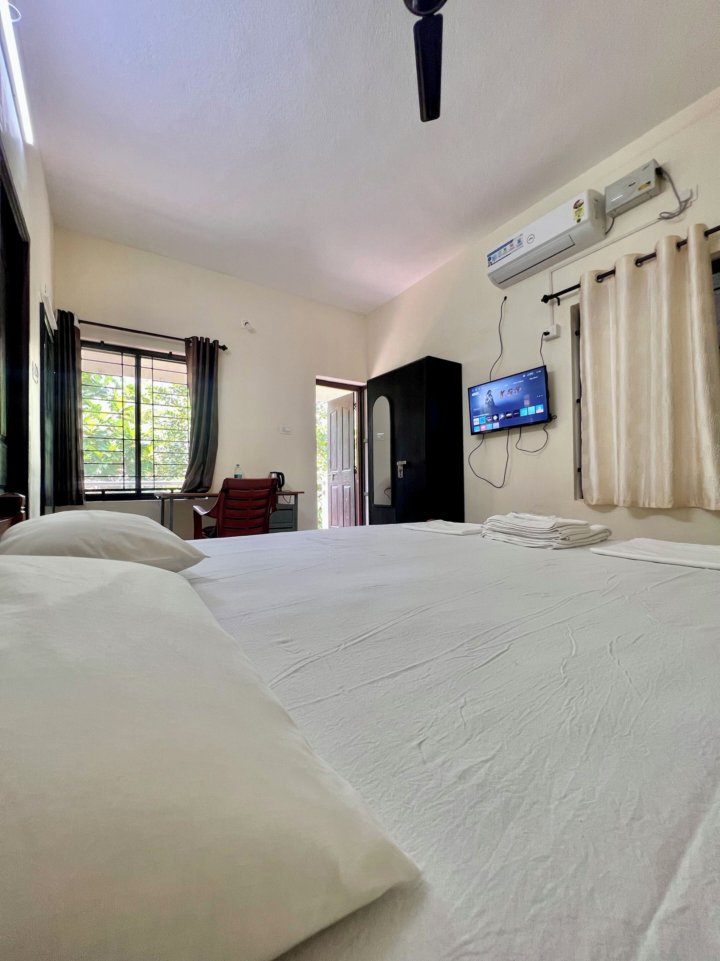 A hotel room with a large bed, a TV mounted on the wall, and a window with curtains.